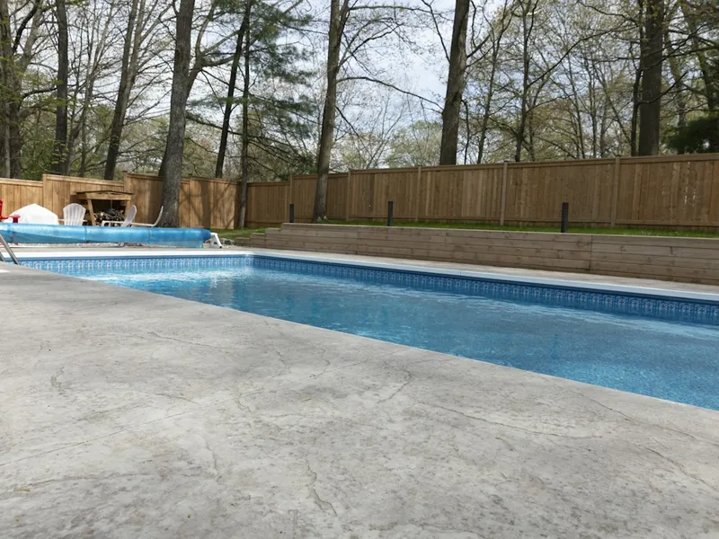 Freshly cleaned backyard pool with a concrete deck and wood fence in San Marcos